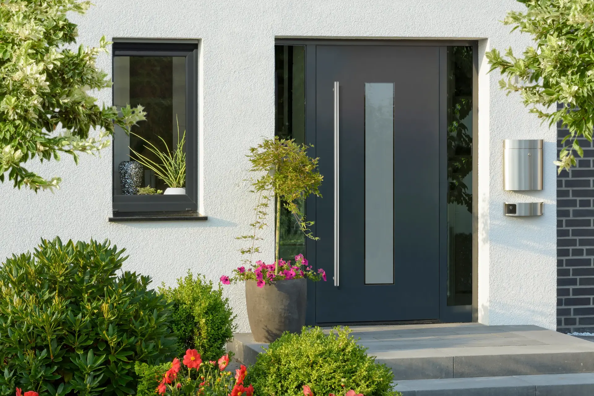 Anthrazitfarbene Haustür mit Glas-Seitenteil und langem Edelstahlgriff an einer weißen Fassade