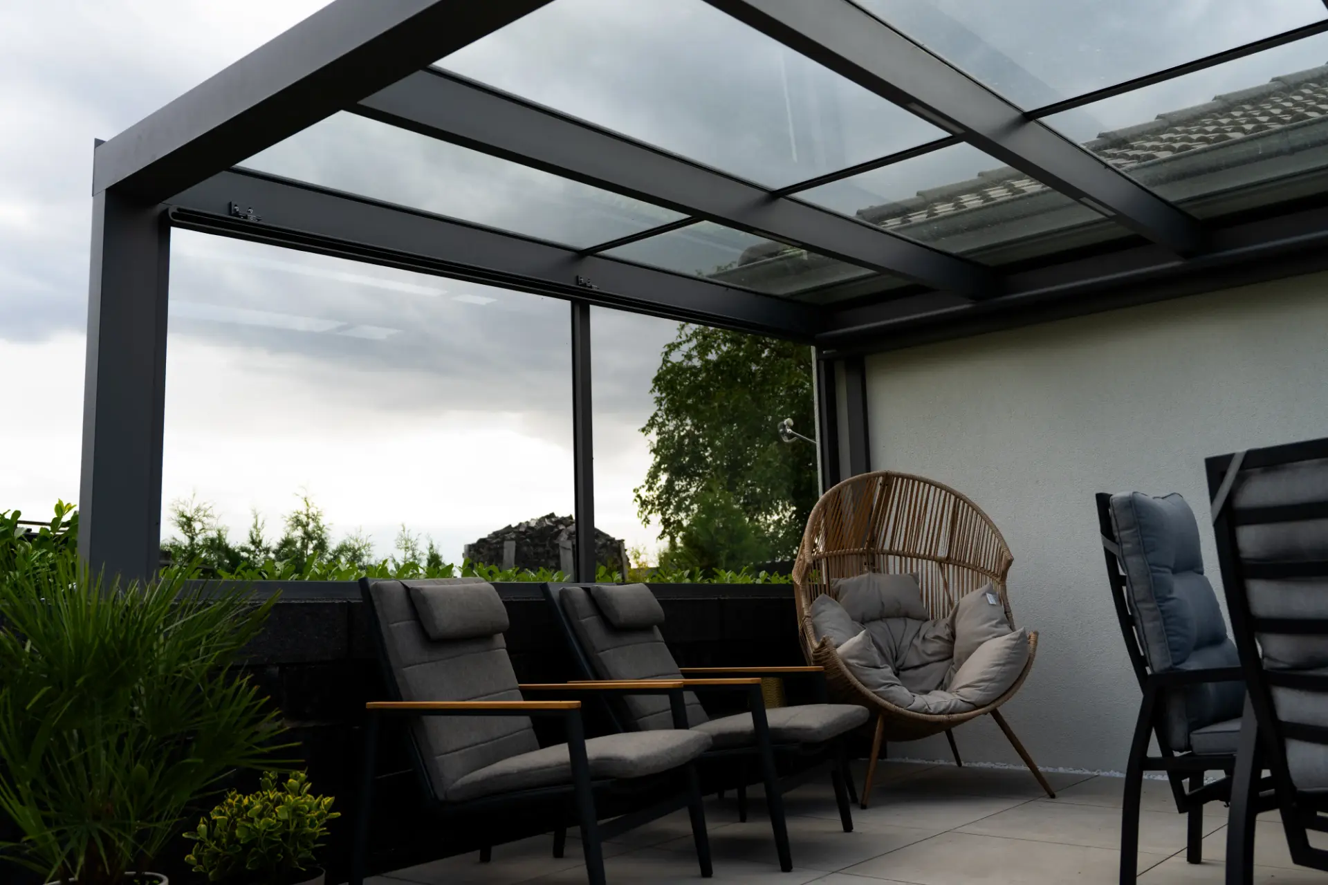 Blick unter ein Terrassendach aus Glas auf Loungesessel und einen Kokon-Sessel